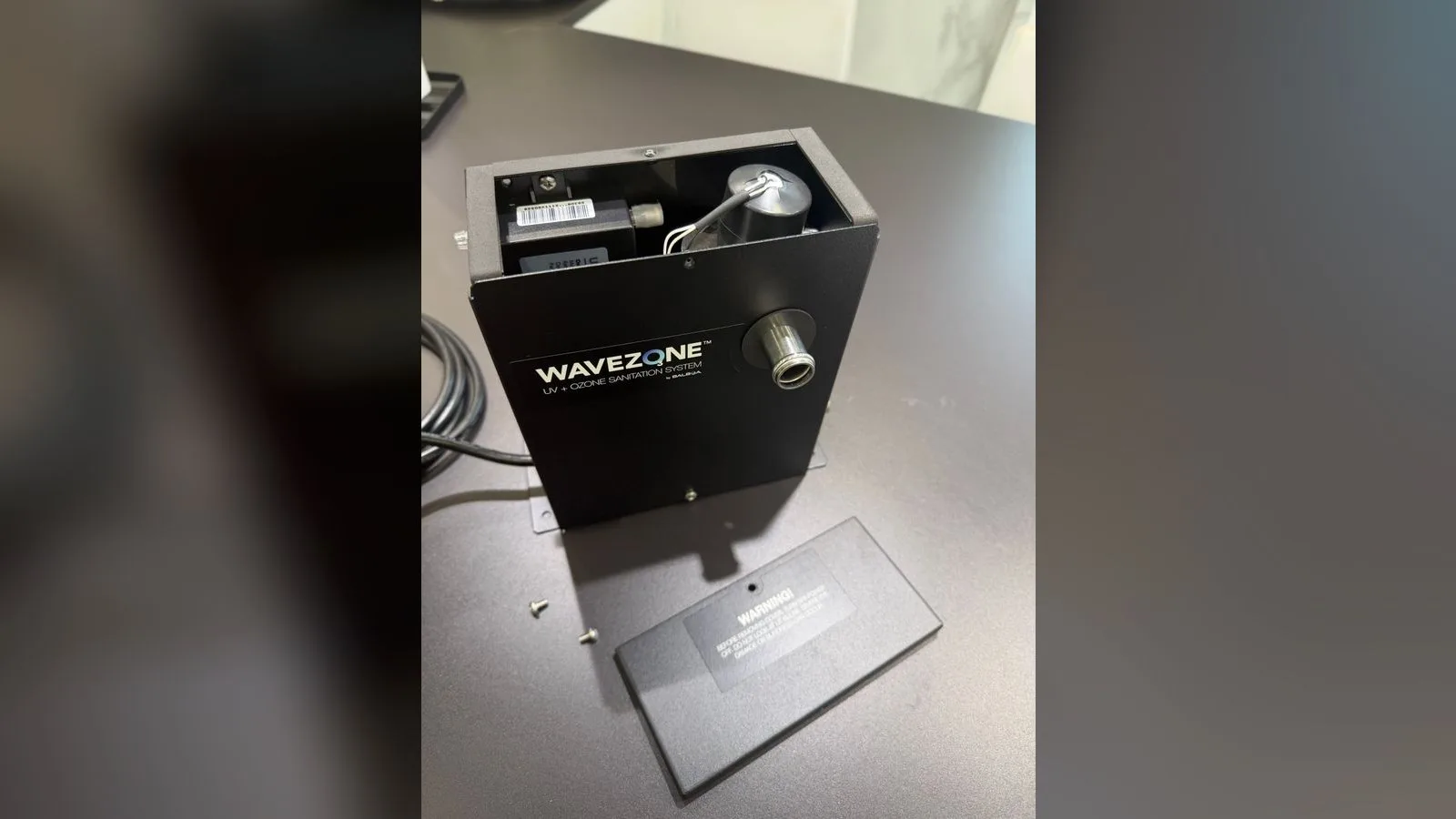 Boîtier Wavezone ouvert, capot posé à côté avec ses deux vis : à l'intérieur, le transformateur à gauche et le capuchon noir de la lampe à droite