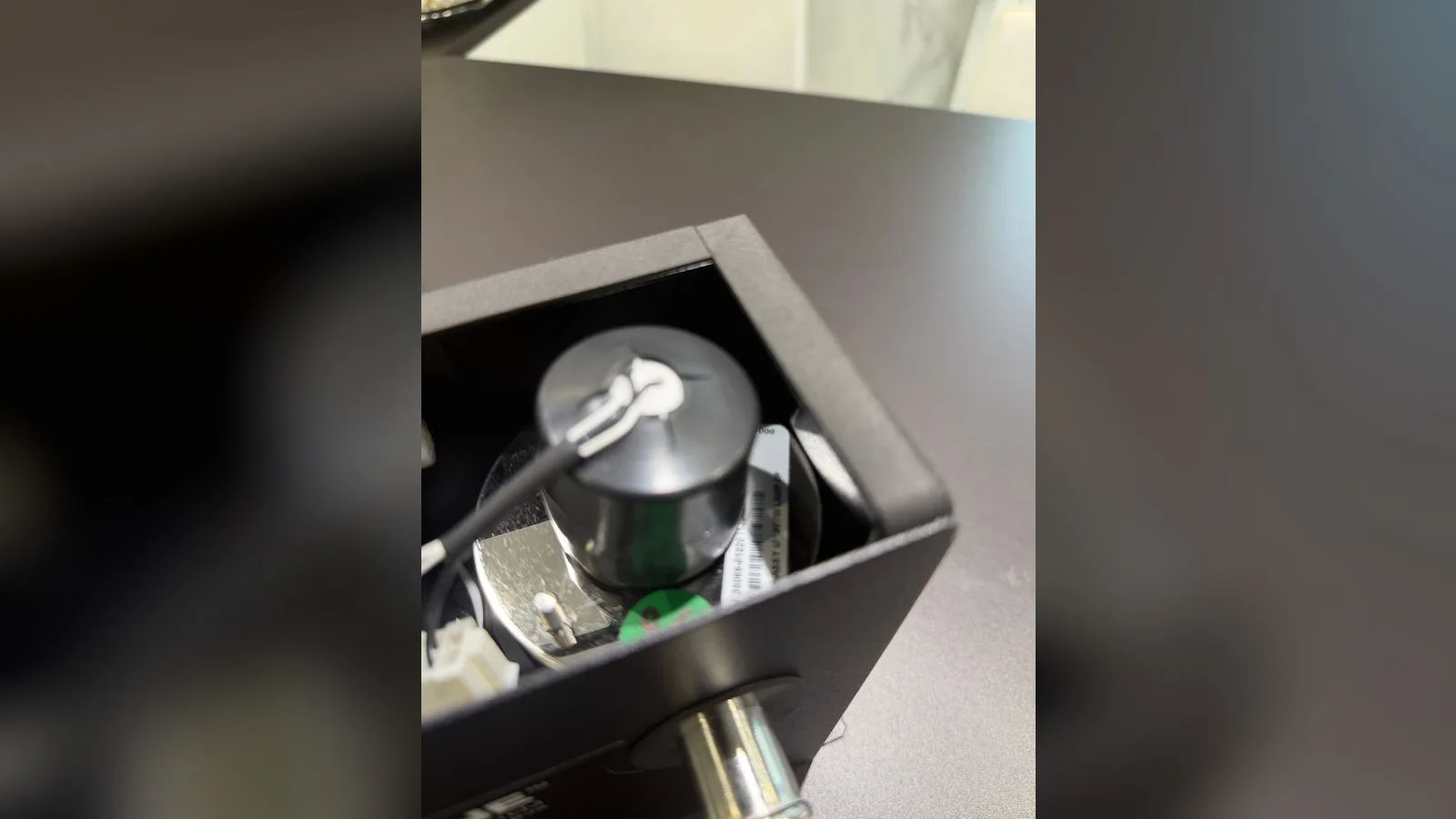 Prise blanche de la lampe débranchée, tenue entre deux doigts au-dessus de sa partie fixe à six trous restée dans le boîtier